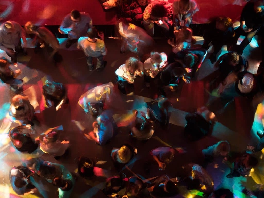 Pessoas dançando em uma pista de night club com luzes coloridas.